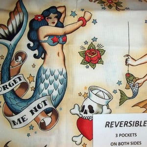 May include: Fabric with a vintage tattoo-style design featuring mermaids, roses, stars, and a skull with a sailor hat. The mermaid has blue hair and a star-shaped bikini top. The words "FORGET ME NOT" are on a banner.