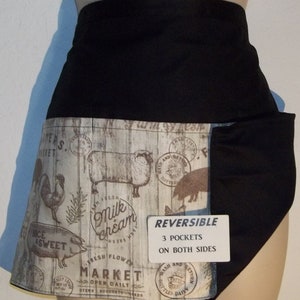 May include: A reversible black apron with a farmhouse-themed print featuring a sheep, rooster, pig, and the text "Fresh Milk Cream". The apron has three pockets on both sides and the text "REVERSIBLE 3 POCKETS ON BOTH SIDES".