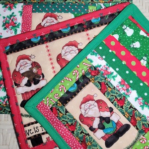 May include: A collection of Christmas-themed quilted placemats. Each placemat features a unique design with Santa Claus, candy canes, and festive patterns in red, green, and white. The edges are finished with a contrasting green border.