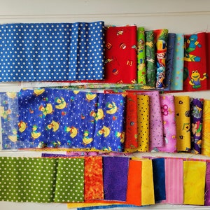 May include: A selection of patterned fabric pieces in a variety of colours. Designs include polka dots, cartoon characters, and floral prints. The fabrics are arranged in rows, showcasing colours like blue, red, green, and yellow. Suitable for quilting or craft projects.