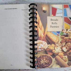 May include: Open cookbook with a spiral binding, featuring a page with the heading "Vegetables" and a blank recipe section. The right page displays a colorful illustration of various breads, rolls, and pastries, with the text "Breads Rolls Pastries".