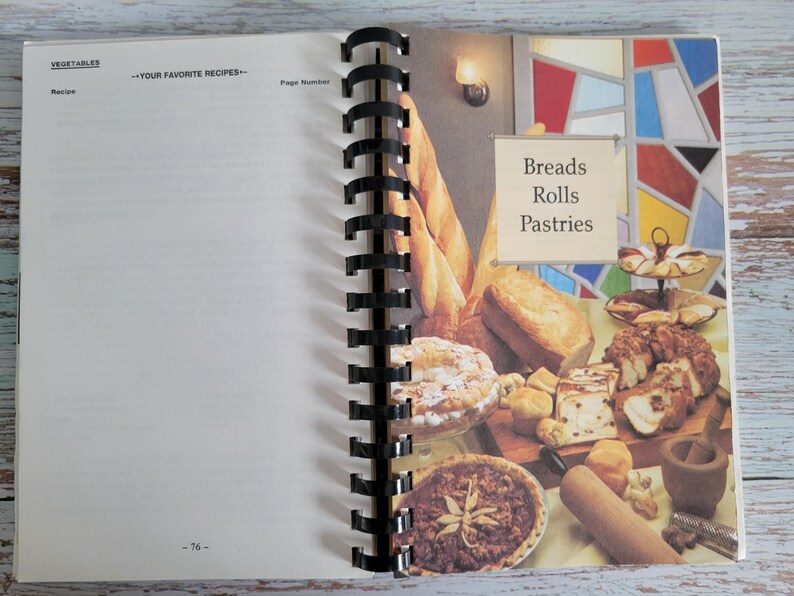 May include: Open cookbook with a spiral binding, featuring a page with the heading "Vegetables" and a blank recipe section. The right page displays a colorful illustration of various breads, rolls, and pastries, with the text "Breads Rolls Pastries".