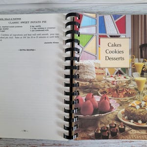 May include: Open cookbook page with a recipe for Classic Sweet Potato Pie. The right page displays a variety of cakes, cookies, and desserts. The text "Cakes, Cookies, Desserts" is visible. The book is spiral-bound.