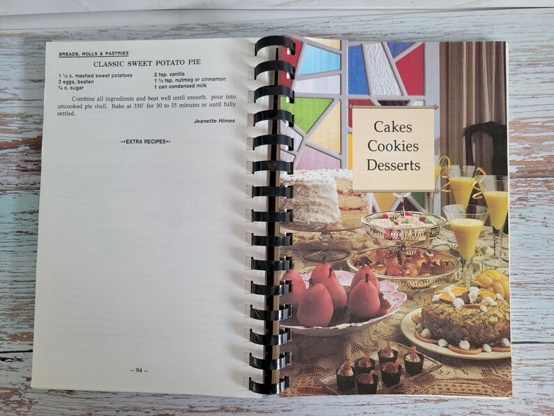 May include: Open cookbook page with a recipe for Classic Sweet Potato Pie. The right page displays a variety of cakes, cookies, and desserts. The text "Cakes, Cookies, Desserts" is visible. The book is spiral-bound.