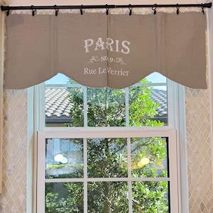 May include: A brown valance with white embroidery that reads "PARIS No.9 Rue Le Verrier" hangs above a white window with a view of green trees and a tiled roof.