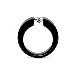 Pode incluir: Um anel preto com acabamento liso e polido, apresentando uma banda circular larga que &eacute; aberta no topo. Uma &uacute;nica pedra preciosa transparente em forma de pera est&aacute; engastada horizontalmente entre as duas extremidades da banda.