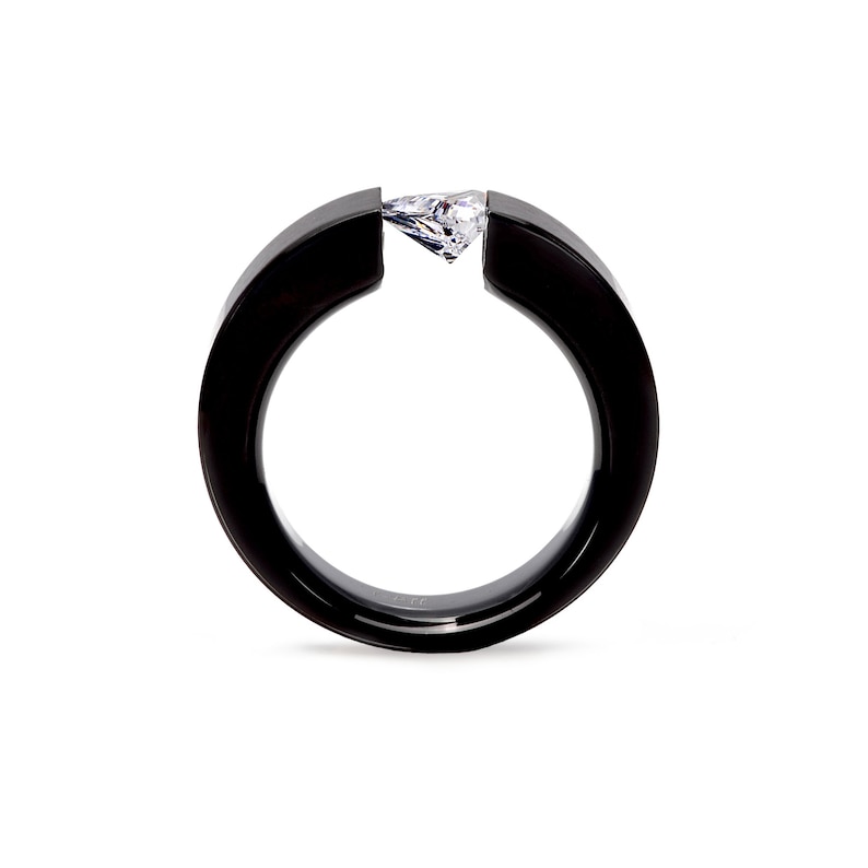 Pode incluir: Um anel preto com acabamento liso e polido, apresentando uma banda circular larga que &eacute; aberta no topo. Uma &uacute;nica pedra preciosa transparente em forma de pera est&aacute; engastada horizontalmente entre as duas extremidades da banda.