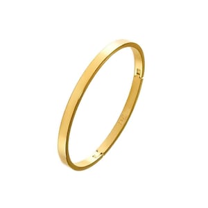 May include: A gold-coloured bangle bracelet with a flat, rectangular design. The bracelet has a hinge closure and a small inscription. The jewellery is set against a white background.