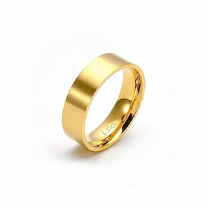 May include: A gold-colored band ring with a smooth, matte exterior finish and a polished, reflective interior surface. The inside of the ring features the engraved text b.titt in a cursive script font, visible against the bright metallic gold tone.