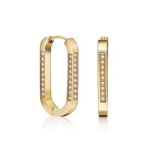 May include: A pair of gold-colored hoop earrings. Each earring has a rectangular shape with rounded corners. Small, clear gemstones are set along the inner and outer edges of the hoops, adding sparkle. The earrings are displayed against a white background.