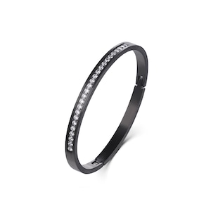 May include: A matte black metal bangle bracelet featuring a single row of small, clear, round-cut stones embedded along the top surface. The bracelet has a hinged clasp mechanism on one side and a smooth, solid finish on the inner band.