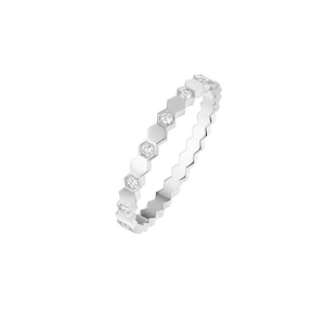 Puede incluir: Un anillo plateado con un diseño hexagonal repetido. Cada hexágono presenta una pequeña gema transparente. El borde del anillo tiene un borde festoneado. El anillo está sobre un fondo blanco.
