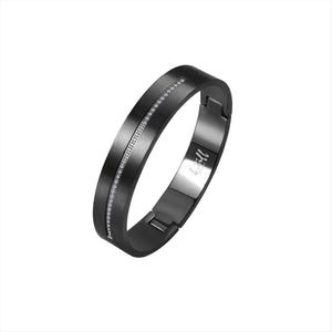 Puede incluir: Una pulsera articulada de color negro mate con un canal central vertical engastado con una hilera de pequeñas piedras transparentes. El interior de la banda muestra el texto grabado "le still" en cursiva, visible cerca de la bisagra.