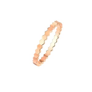 Puede incluir: Un anillo de oro rosa con un patrón hexagonal repetido. El anillo es una banda delgada, y el diseño geométrico le da un aspecto moderno y elegante. El anillo se muestra sobre un fondo blanco.