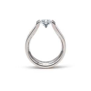 Könnte beinhalten: Ein silberner Ring mit einem großen, klaren Diamanten in einem einzigartigen, offenen Design. Das Band verläuft nach oben, um den Diamanten zu umschließen, was einen modernen und eleganten Look erzeugt. Der Ring ist vor weißem Hintergrund.