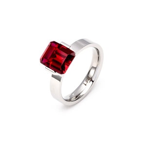 May include: A silver ring with a large, red, emerald-cut gemstone.