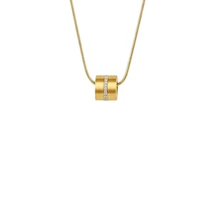 May include: A gold-colored necklace with a cylindrical pendant. The pendant has a band of small, clear stones encircling the center. The chain is a thin, gold-colored snake chain. The jewelry is set against a white background.
