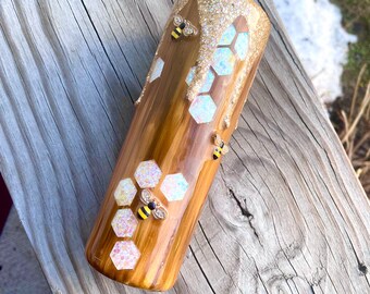 May include: A brown and gold tumbler with a honeycomb design and glitter accents. There are three small bee figurines attached to the tumbler.