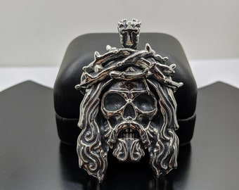 May include: Silver pendant featuring a skull with a crown of thorns and a beard. The pendant is in a black velvet box.