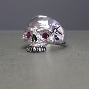 May include: A silver skull ring with two red gemstone eyes.