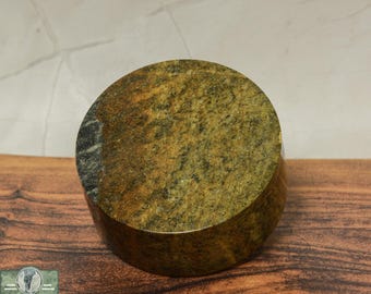 Puede incluir: Un posavasos redondo de mármol verde y marrón con una banda verde oscuro alrededor del borde. El posavasos está sobre una superficie de madera.