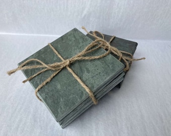 Puede incluir: Conjunto de cuatro posavasos cuadrados de pizarra atados con cuerda. Los posavasos son de color verde oscuro con un patrón moteado.