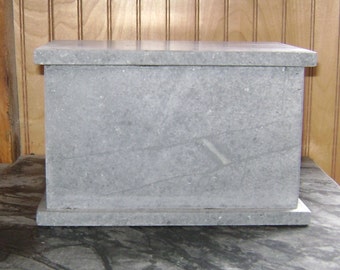 Puede incluir: Una caja de piedra gris con tapa. La caja está hecha de piedra natural y tiene una textura rugosa.