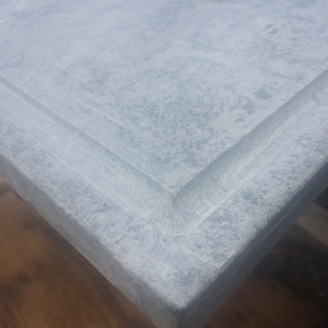 May include: A close-up of a light gray concrete countertop with a slightly raised edge. The surface has a subtle, speckled texture.