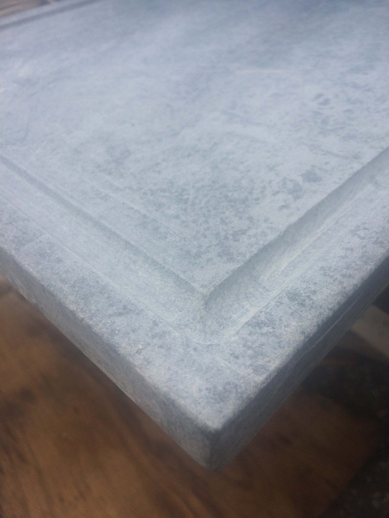 May include: A close-up of a light gray concrete countertop with a slightly raised edge. The surface has a subtle, speckled texture.