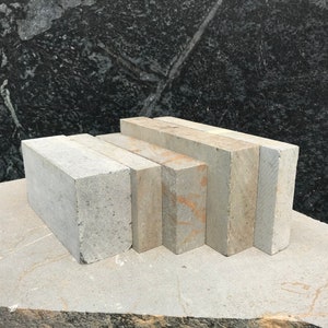May include: A stack of five rectangular grey stone tiles, with a slightly rough texture, arranged in a graduated size from largest to smallest. The tiles are sitting on a grey stone surface.