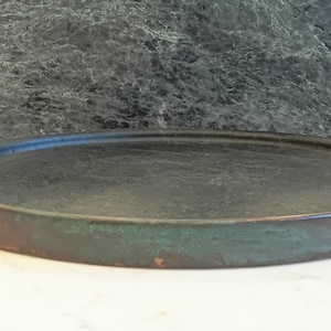 May include: A round copper serving tray with two handles. The tray has a dark green patina and a copper rim.