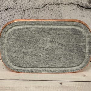 May include: A rectangular slate serving tray with copper-colored handles. The tray is made of natural stone and has a smooth, polished surface.