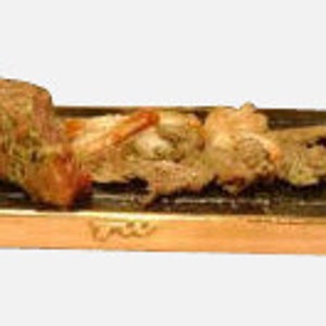 May include: A copper-colored rectangular serving tray with a black stone insert. The tray has two handles and features a small inscription on the front. The stone insert is filled with cooked meat and vegetables.