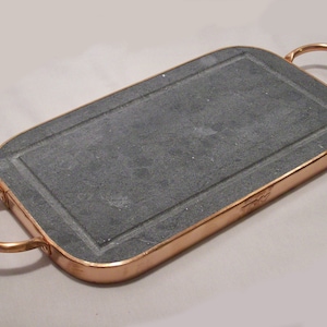 May include: A rectangular slate serving tray with copper trim and two copper handles. The tray is made of natural slate and has a rustic look.
