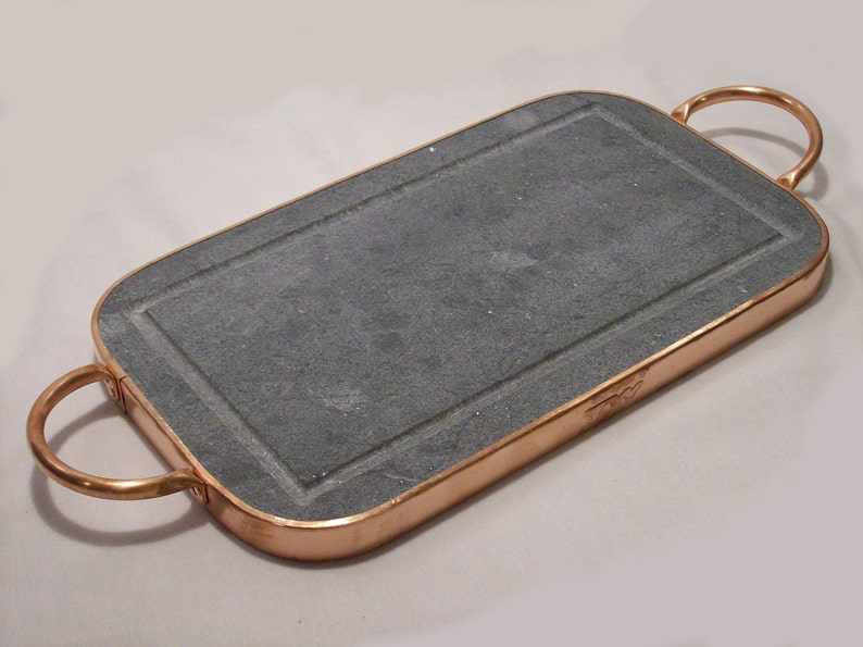 May include: A rectangular slate serving tray with copper trim and two copper handles. The tray is made of natural slate and has a rustic look.