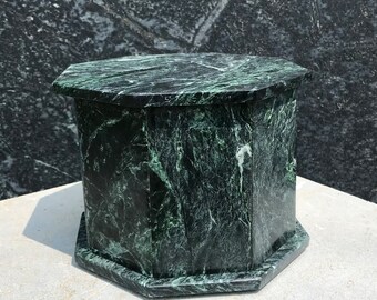 Puede incluir: Pedestal octogonal de mármol verde con una superficie lisa y pulida. El pedestal tiene un color verde oscuro con vetas blancas.