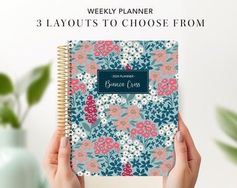 May include: A blue weekly planner with a floral pattern in pink, white, and red. The planner has a gold spiral binding and the text "2023 Planner - Bianca Cross" on the front cover.