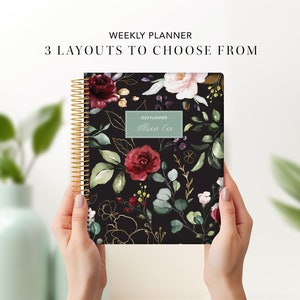 May include: A black weekly planner with a floral design featuring red, pink, and green flowers and gold accents. The planner has a spiral binding and a personalised name tag that says "Alison Lee".