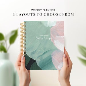 May include: A weekly planner with a green, pink, and white abstract design. The planner has a gold spiral binding and says "2023 Planner - Stacey Vargas" on the front cover.