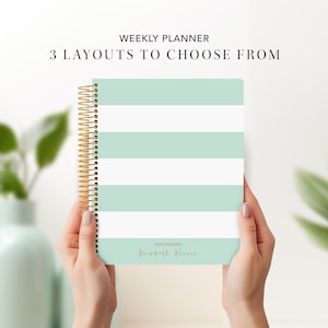 May include: A mint green and white striped weekly planner with gold spiral binding. The planner has the text "2023 Planner" and "Kendall +  Paris" on the front cover.