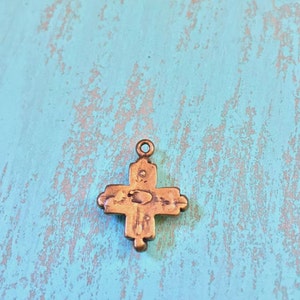 May include: A small, antique-looking, gold-toned cross pendant with intricate details. The cross has a slightly worn, aged appearance.