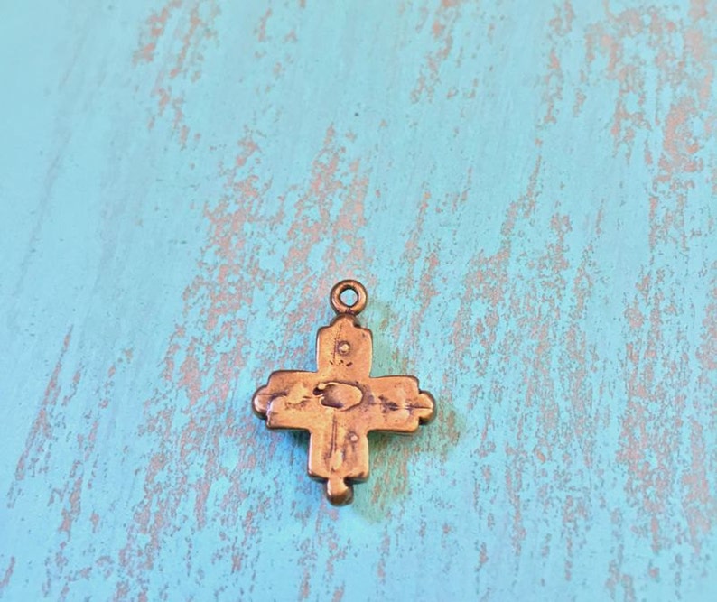May include: A small, antique-looking, gold-toned cross pendant with intricate details. The cross has a slightly worn, aged appearance.