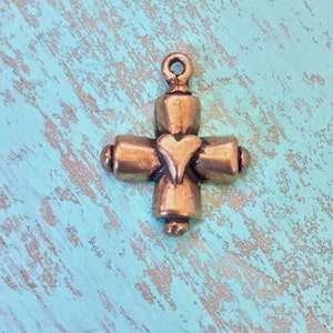 May include: A small, gold-toned metal cross charm with a heart in the center. The cross has a simple design with rounded edges.