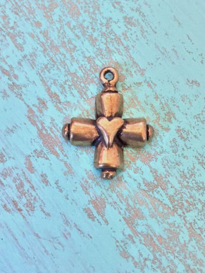 May include: A small, gold-toned metal cross charm with a heart in the center. The cross has a simple design with rounded edges.