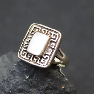 May include: A silver ring with a square-shaped white stone set in a geometric design.