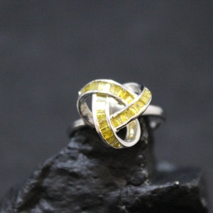 May include: A silver ring with a knot design and yellow gemstones.