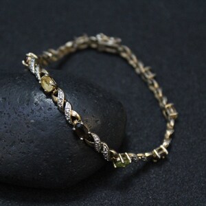 May include: A gold chain bracelet with a twisted design and alternating green, yellow, and black gemstones.