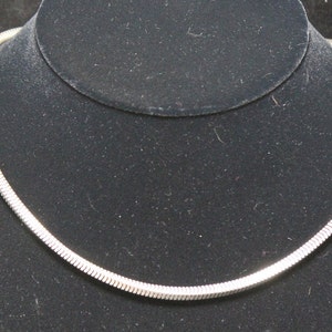 May include: A silver snake chain necklace on a black velvet display stand.