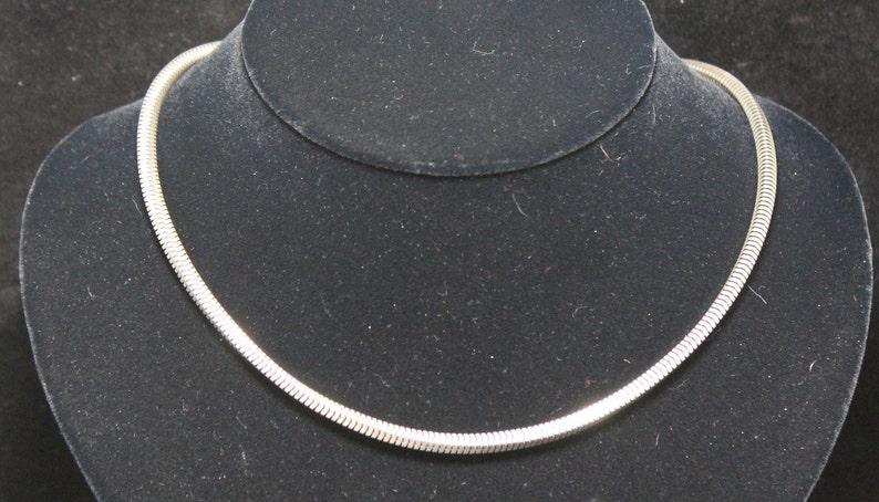 May include: A silver snake chain necklace on a black velvet display stand.
