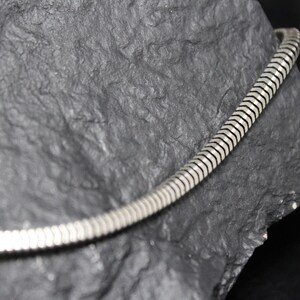 May include: A silver snake chain necklace with a smooth, shiny finish. The chain is made of small, interlocking links that create a flexible and comfortable fit.